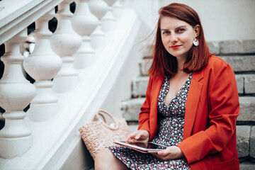 Businesswoman in stylish clothes working uses modern tablet device while sitting on the street