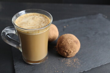 cappuccino coffee with foam and dessert cake chocolate candy in cocoa on a black stone background side view. delicious breakfast