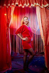 Young woman during a stylized theatrical circus photo shoot in a beautiful red location. Girl...