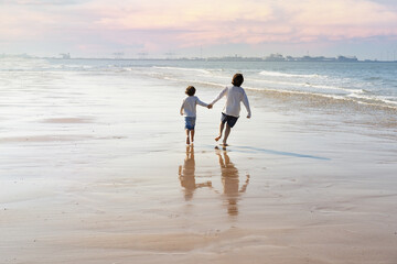 Two happy brothers holding hands are running along the seashore at the North Sea. Boys spending weekend at the  seaside in Belgium, Knokke. Siblings friendship concept.