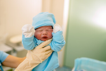 The doctor hands in glaves holding the just born baby boy dressed in clothes for newborns in...