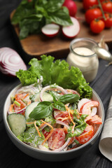 Bowl of delicious vegetable salad dressed with mayonnaise and ingredients on black table