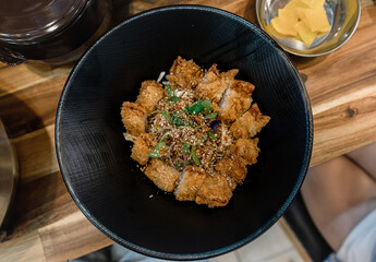 Pork cutlet over rice in a black bowl.
