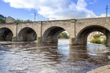 Fototapeta na wymiar A beautiful old bridge going over the River Wharfe in the British town of Wetherby in Leeds, West Yorkshire in the UK, showing the stone brick bridge going in to the village on a hot sunny summers day