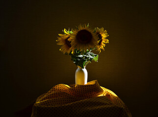 Dark still life with sunflowers, illuminated from behind by sunlight