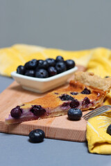 Slice of Blueberry tart on wooden cutting board. Sweet blueberry cake on a table. Homemade dessert close up photo. Healthy eating concept. Grey background with copy space. 