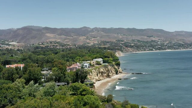 Beautiful lavish tropical nature of Malibu coastline. Aerial of high sea cliff with luxury property, residential mansions with epic Pacific ocean views. Waterfront houses on the edge of rocks, Malibu