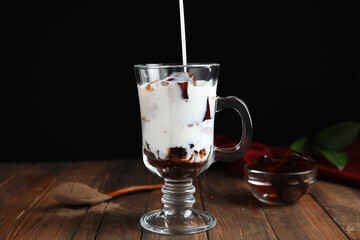 Pouring milk into glass cup with delicious grass jelly at wooden table