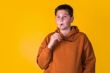 handsome boy with glasses in a brown sweatshirt on a yellow background