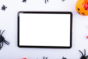 Composition of halloween spiders, pumpkin and sweets and tablet with copy space on white background