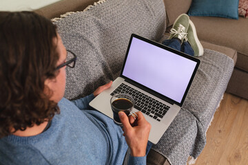 Rear view of disabled man holding coffee cup using laptop with copy space on couch at home