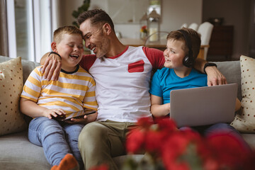 Portrait of caucasian father and two sons with laptop and digital tablet smiling at home