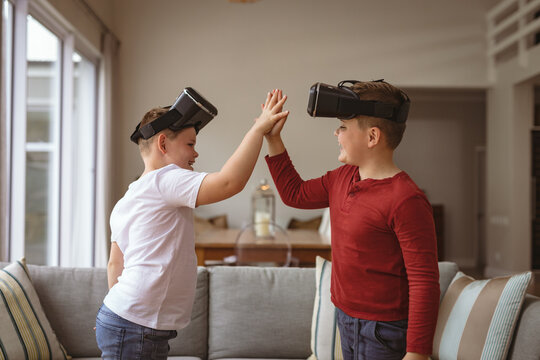 Two caucasian boys wearing vr headsets high fiving each others at home