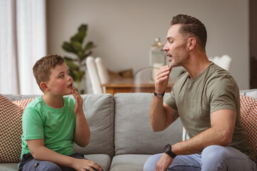 Caucasian father and son communicating using sign language while sitting on the couch at home