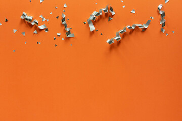 close up on group of silver color of rolling ribbon and confetti on panoramic orange background...