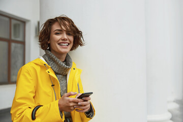 Woman in yellow raincoat with smartphone in hand
