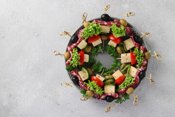 Obraz na płótnie Canvas Festive canapes with sausage, cucumbers, tomatoes, olives and cheese, served on a plate as a Christmas wreath, on a light background. Top view
