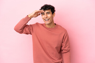 Young Argentinian man isolated on pink background looking far away with hand to look something