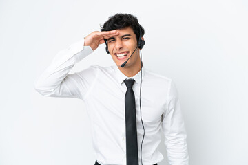 Telemarketer man working with a headset isolated on white background looking far away with hand to look something
