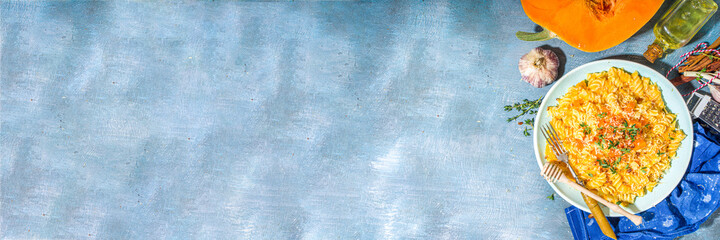 Creamy cheesy vegan pumpkin pasta, fusilli with pumpkin squash sauce, cheese and thyme, on concrete blue table background copy space