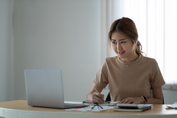 portrait of smiling woman making notes while taking part in webinar at tabletop with laptop in office