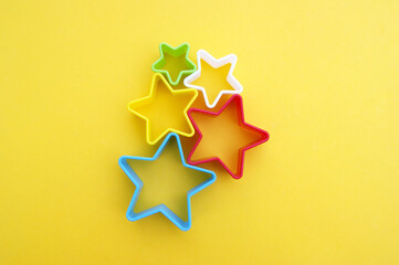 Plastic molds of multi colors for making cookies in the shape of a star on a yellow background.