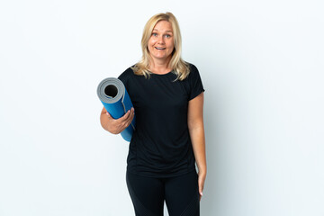 Middle age woman going to yoga classes while holding a mat isolated on white background with surprise and shocked facial expression