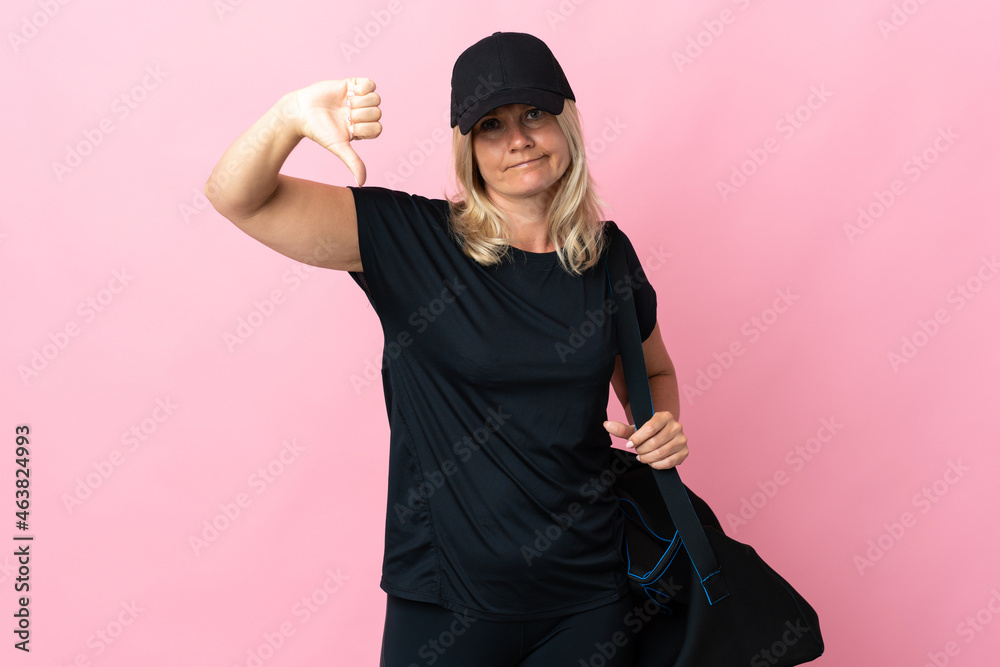 Wall mural Middle age woman with sport bag isolated on pink background showing thumb down with negative expression