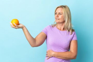 Middle age Lithuanian woman isolated on blue background holding an orange