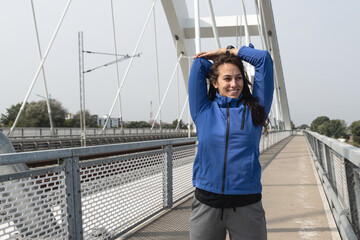 Obraz premium Young beautiful happy sporty fitness woman standing on the bridge stretching her muscles preparing for jogging and running exercise while she concentrate for workout and training marathon motivation