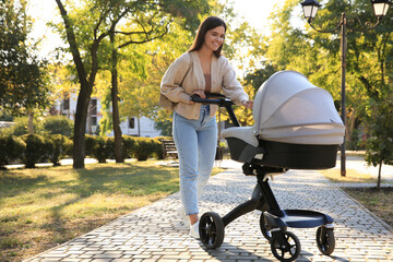 Young mother walking with her baby in stroller at park on sunny day