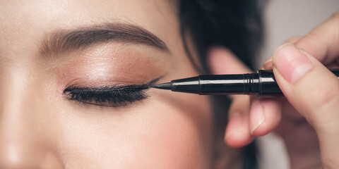 Make-up artist brush black eyeliner on the face of the woman. - obrazy, fototapety, plakaty