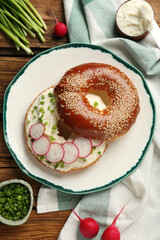Delicious bagel with cream cheese, green onion and radish on wooden table, flat lay