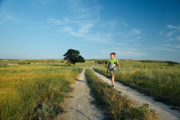 Boy walking among filds and hills and  looking something by the hand and points to the sky into the distance