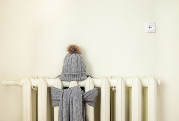 Vintage heating radiator with wool knitted winter hat and scarf. The electricity and gas bill goes...