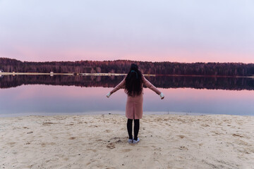 brunette girl stands by the lake during sunrise or sunset