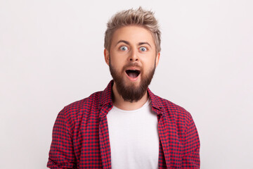 Portrait of extremely surprised caucasian bearded man looking at camera with open mouth and big eyes, happy satisfied with good cashback. Indoor studio shot isolated on gray background