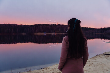 brunette girl stands by the lake during sunrise or sunset
