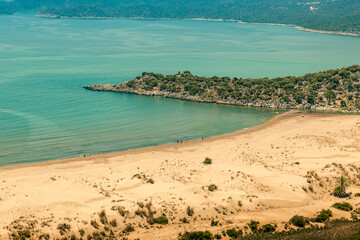 View of a wild sandy beach with a small ridge jutting into a bay on the Mediterranean coast with turquoise-blue water and a mountain landscape in the background