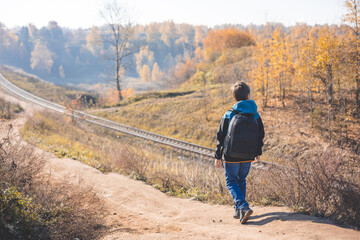 Teenager boy with backpack walking on path in autumn park. Active lifestyle, Back to school. Rear view of student boy in fall forest. People from behind