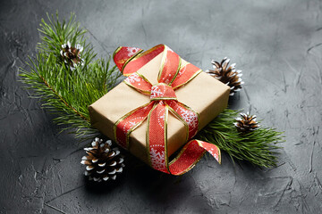 Gift box with red ribbon and green Christmas tree branch with pine cones on black
