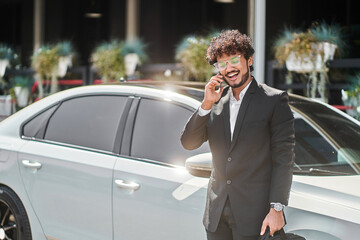 curly-haired Indian businessman talking on the phone in front of the car