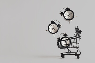 Toy shopping cart with three levitating alarm clocks on gray background with copy space. Black Friday banner, shopping concept.