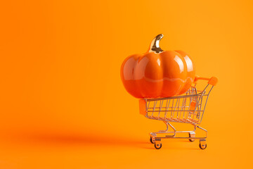 Toy shopping cart with big pumpkin on orange background with copy space. Halloween banner, shopping concept.