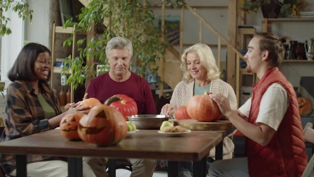 A couple of retirees and a girl are sitting at the table and listening to a pumpkin carving masterclass