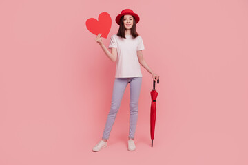 Photo of cheerful romantic lovely lady hold umbrella showing red heart figure isolated pink color...
