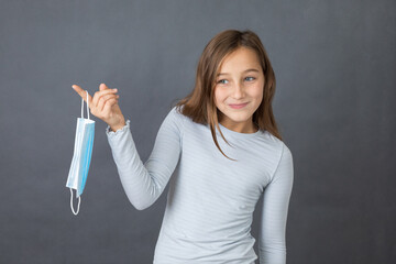 Portrait of a young happy girl playing with medical mask on grey background. - 463842777