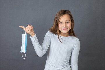 Portrait of a young happy girl playing with medical mask on grey background. - 463842780