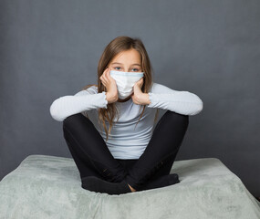 Portrait of a young teen girl in a medical mask sitting on the ground with grey background. - 463842785