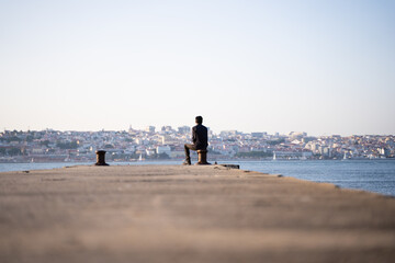 Back of a man sitting facing the river and the city scape in a sunny day